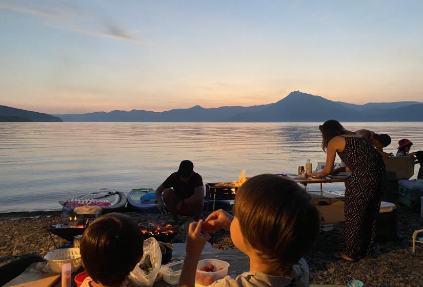 2 children eat at a lakeside campsite at sunset          