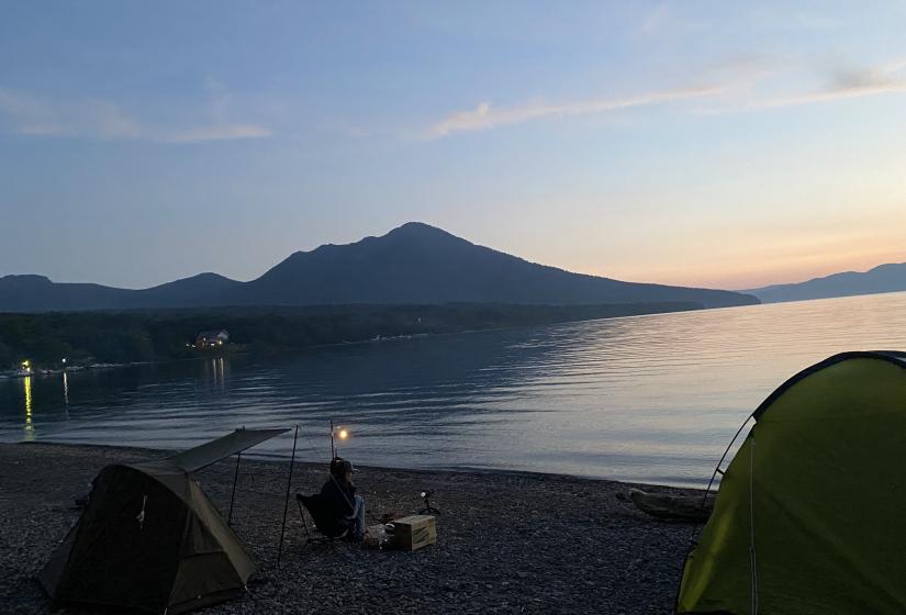 A single camper enjoys a lake view at sunset