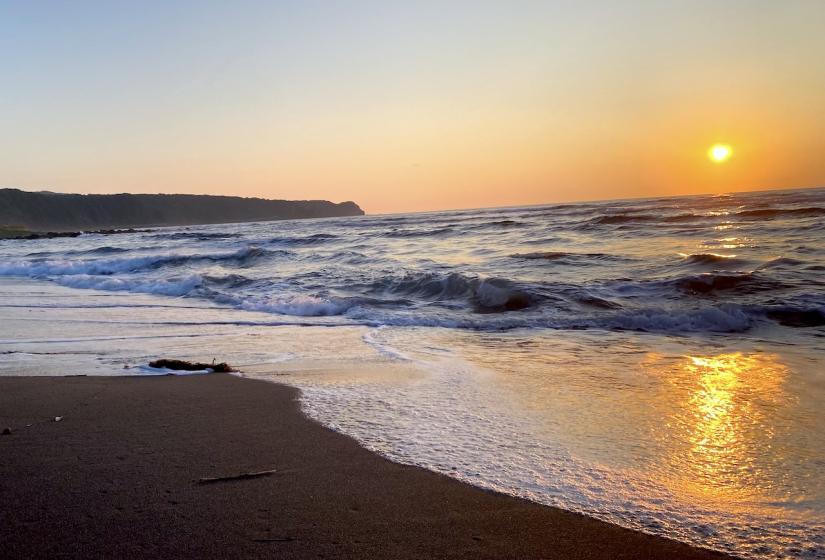 An orange sunset across the waves at a sandy beach.