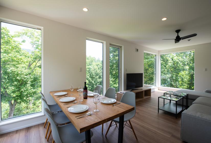 Large windows provide plenty of natural light and beautiful views of the forest surrounds. A table set with plates and wine glasses with large windows with a view to leafy surrounds