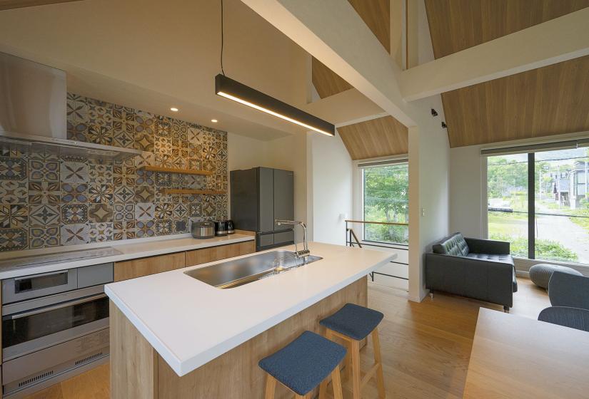 An island bench with kitchen and colourful tiles behind