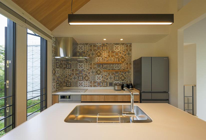 A kitchen sink in an island kitchen with stove top, bench and fridge behind