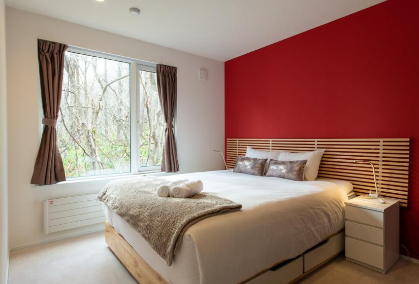 A double bed with brown throw and red wall behind