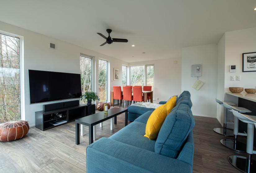 A lounge area with blue sofa and yellow pillows and dining table behind.