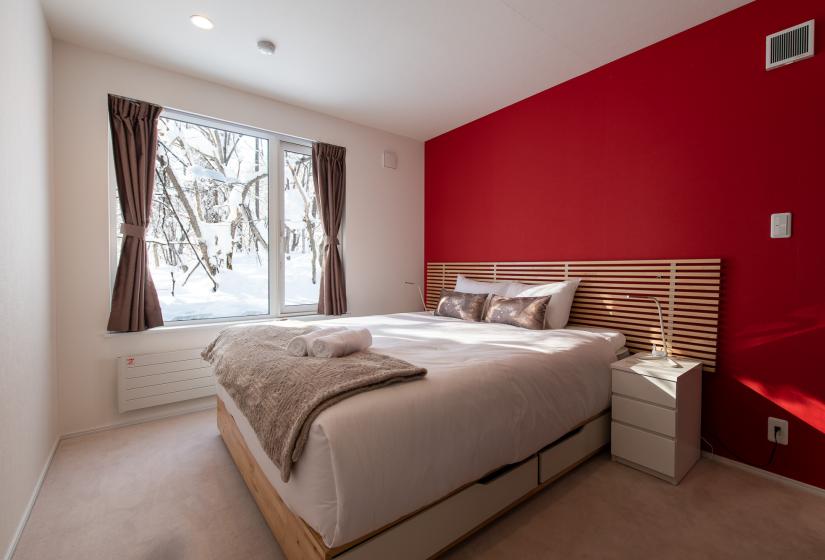 A bedroom with double bed and red wall behind