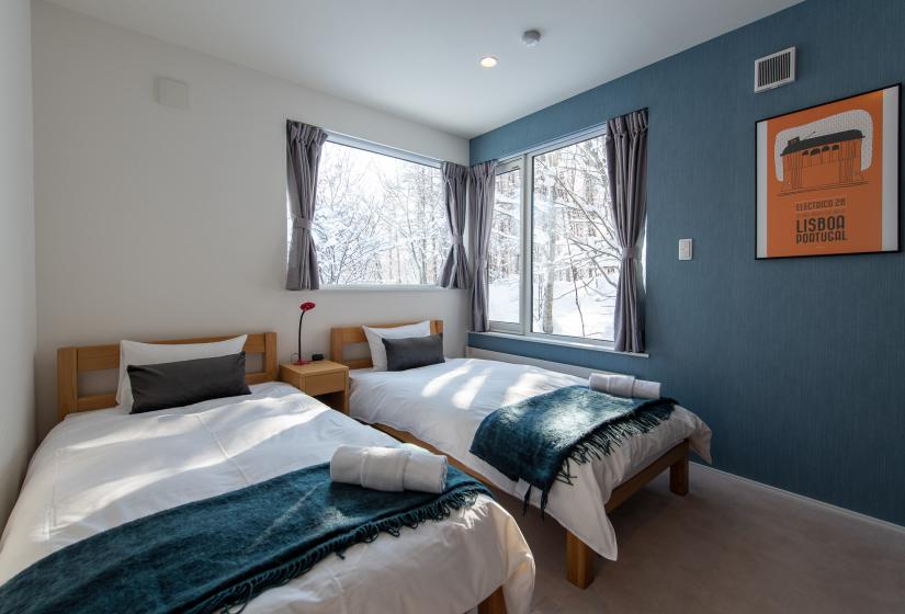 2 single beds with a blue wall and windows beside