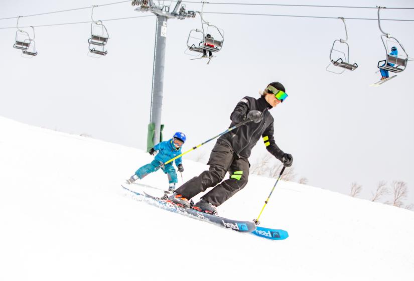 A ski instructor with child skiing down a slope  