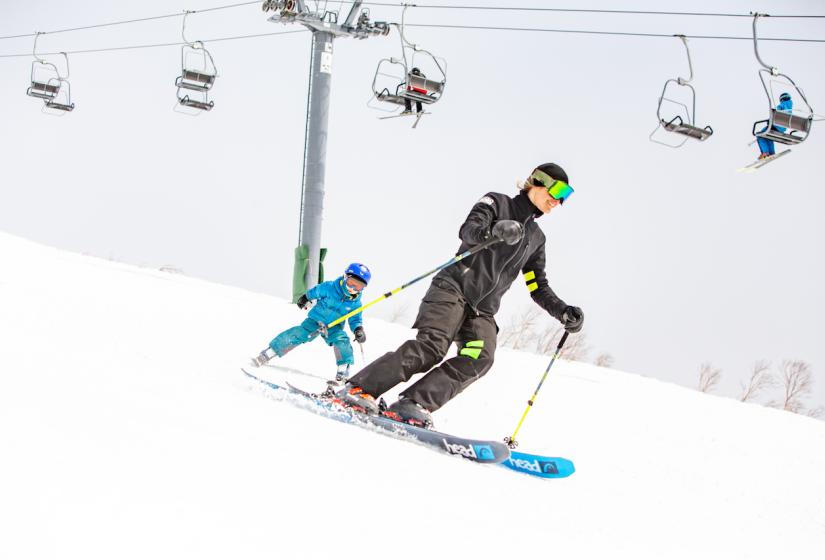 Holiday Niseko and Niseko Black offer complete concierge and luxury accommodation packages. A ski instructor with child skiing down a slope