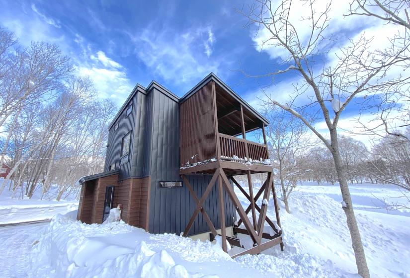 A two story house surrounded by snow with blue sky above