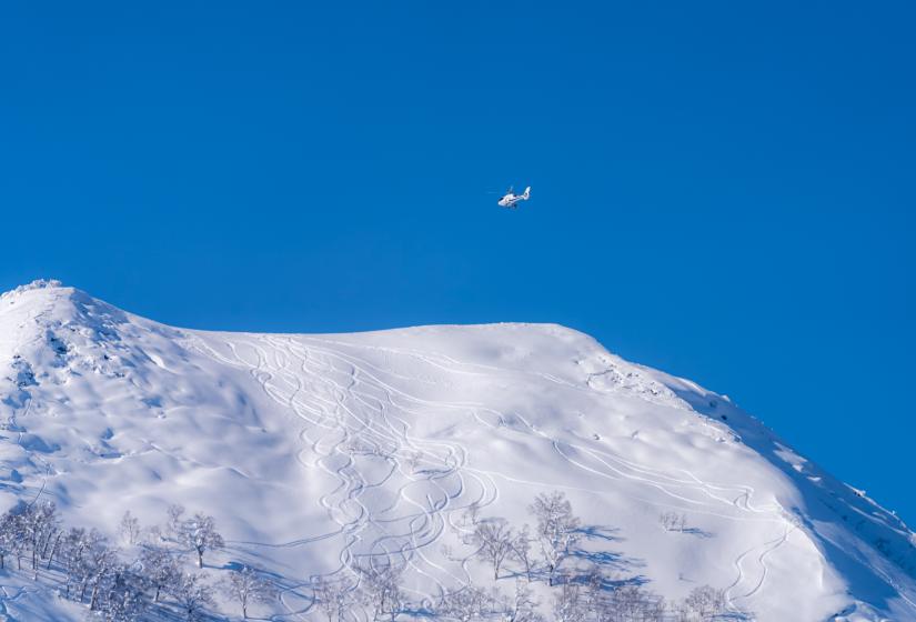 A helicopter flies above Mount Shiribetsu with ski tracks below