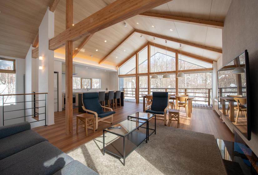 A large living room with exposed beams and wooden floors and kitchen in background