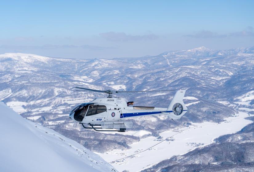 A helicopter comes in to land on a mountainside high above a snow covered landscape.