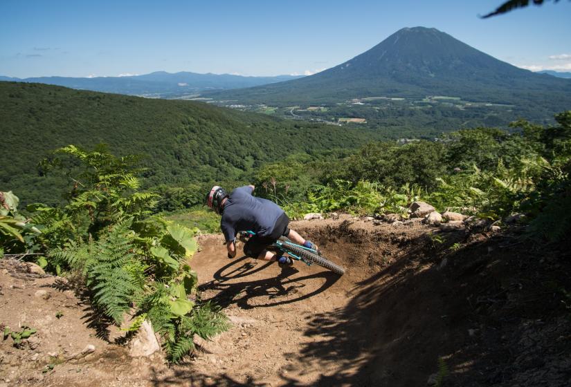 A mountain biker turns through a berm with Mount Yotei in the back ground.