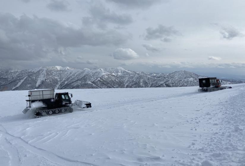 Two snow cats aith mountains in the back ground