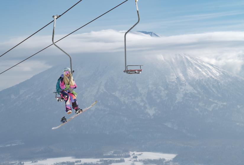 Timeless Niseko imagery for memories you'll never forget. A snowboarder rides a single chair lift