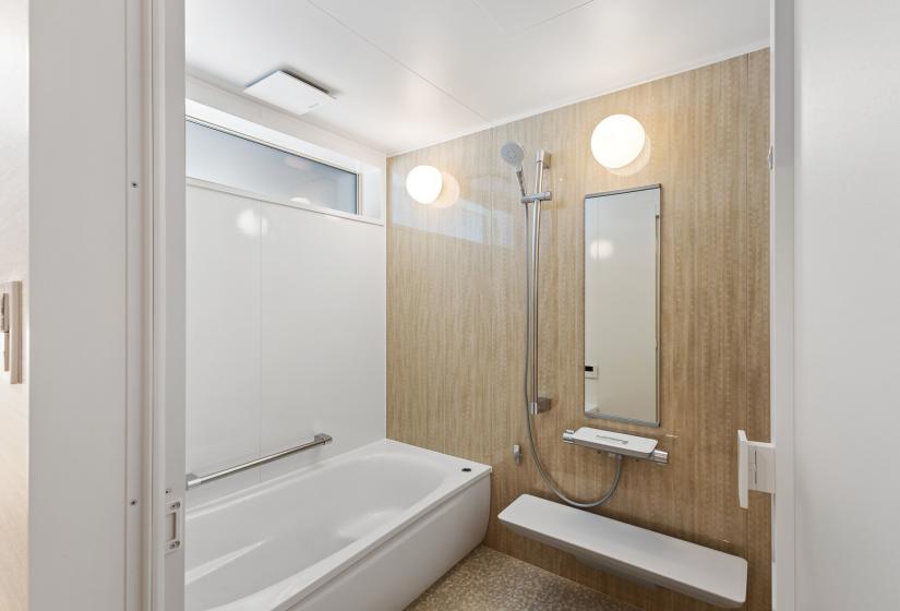 Modern bathroom featuring a full-size bathtub, light wood accent wall, white tile surround, and contemporary globe pendant lights. The clean design combines minimalist white surfaces with warm wood elements