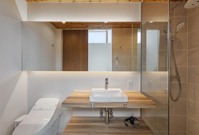 Modern guest bathroom featuring a floating wooden vanity, wall-mounted toilet, and glass shower enclosure. The design combines white walls and fixtures with warm wood accents and minimalist styling