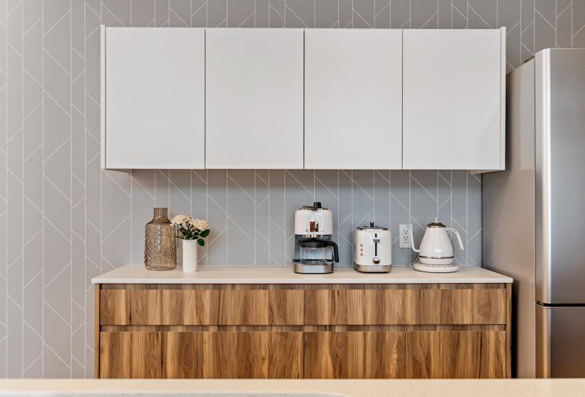Modern kitchen storage featuring white upper cabinets and natural wood lower cabinets, with coffee maker, kettle, and kitchen essentials displayed on the counter. The design combines minimalist white and warm wood elements