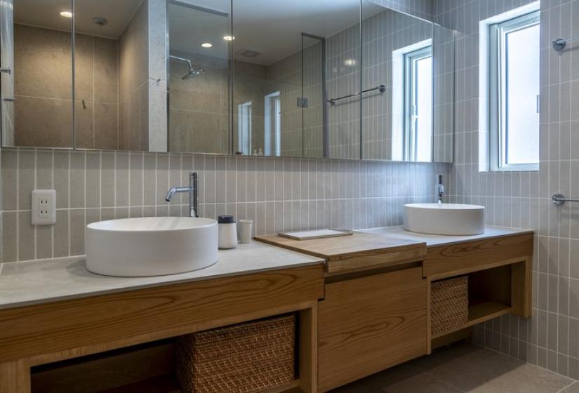 Elegant modern bathroom in Nagare House Niseko featuring dual vessel sinks on a warm wooden vanity, expansive mirror, contemporary gray tiling, and natural light flooding through windows, perfect for luxury ski accommodation in Japan.