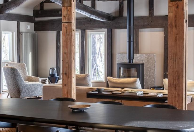  Elegant open-concept kitchen and dining area at Nagare House featuring a wooden breakfast bar with modern pendant lighting, traditional exposed wooden beams and posts, large windows with snowy views, and comfortable dining chairs. This beautifully restored 100-year-old kominka farmhouse combines traditional Japanese architecture with contemporary design elements, perfect for luxury ski accommodation in Niseko.