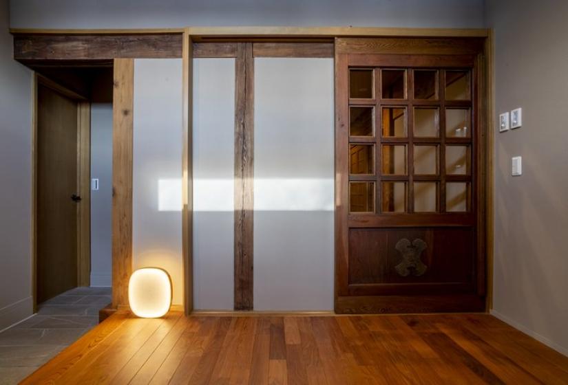 nterior view of Nagare House featuring traditional Japanese-style wooden built-in cabinetry with grid-patterned sliding doors, polished wooden flooring, neutral walls, and a subtle floor lamp creating warm ambient lighting, showcasing the authentic kominka farmhouse elements preserved in this luxury Niseko ski accommodation.