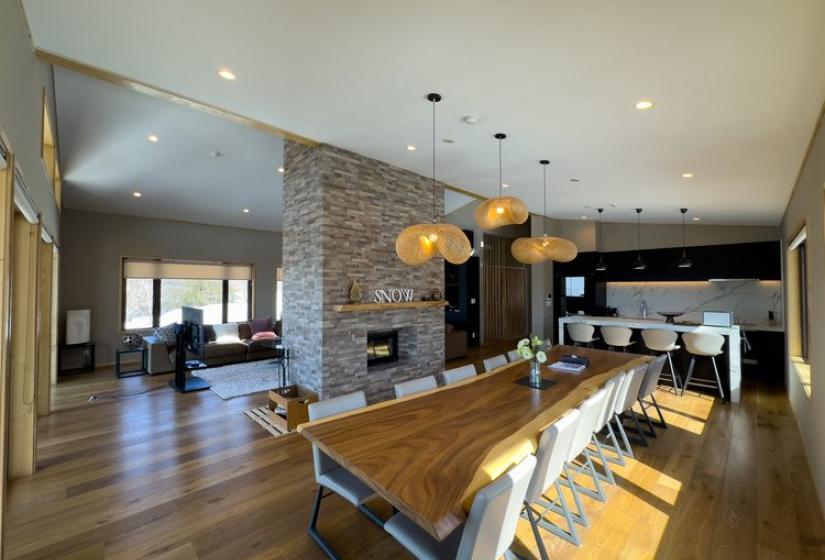 Niseko Chalet Taiko's open-plan dining area featuring long wooden table, stone fireplace, and connected living space
