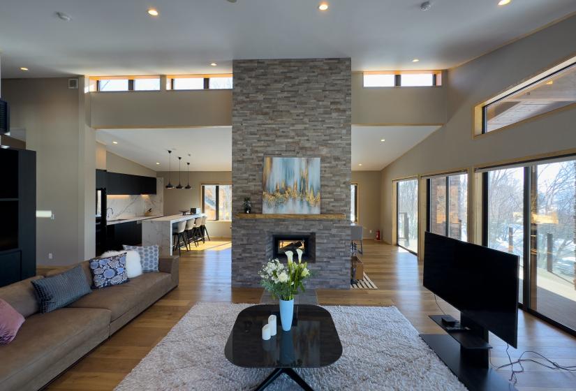 Niseko Chalet Taiko's expansive living room with vaulted ceilings, stone fireplace, and modern furnishings, featuring natural light from clerestory windows