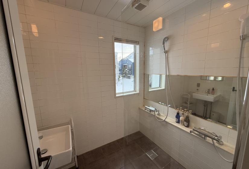Japanese-style bathroom at Yutaka Townhouses featuring deep soaking tub, bright white tiled walls, window with natural light, and modern fixtures, perfect for relaxing after skiing in Niseko.