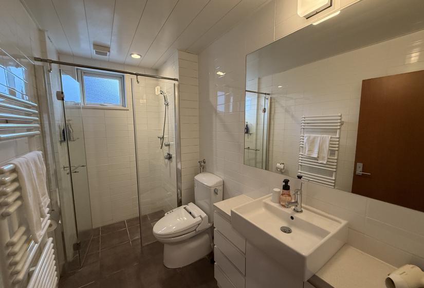 Contemporary bathroom at Yutaka Townhouses featuring glass shower enclosure, white vanity with storage, Japanese washlet toilet, heated towel rack, and modern finishes, providing premium comfort for guests on Niseko ski holidays.