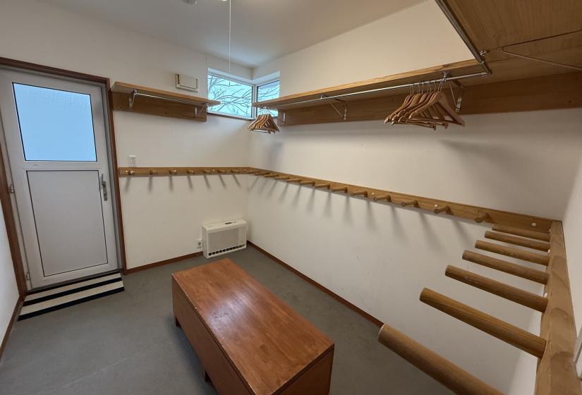 Functional ski drying room at Yutaka Townhouses with wooden wall hooks for equipment, bench seating, entrance doorway, and warm wooden accents, offering practical amenities for storing and drying gear during Niseko ski vacations.