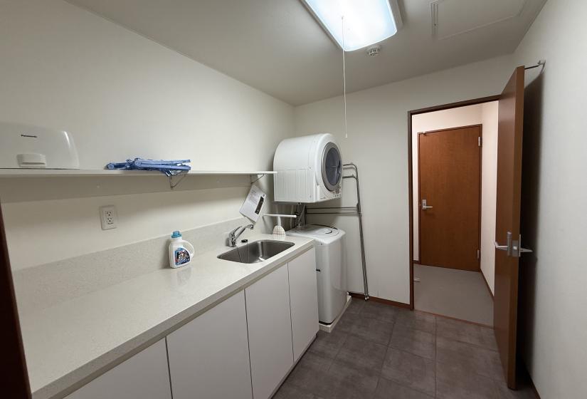 Practical utility room at Yutaka Townhouses featuring white countertop with sink, washing machine, dryer, and ample storage space, providing convenient laundry facilities for guests during extended Niseko ski holidays.