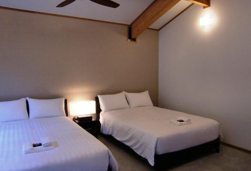 Bedroom with two double beds with white linens, wooden ceiling beams, ceiling fan, and bedside lighting at Chalet Creekside.