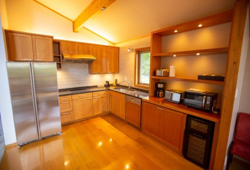 Modern kitchen with wooden cabinetry, stainless steel refrigerator, built-in oven, black countertops, recessed lighting, and polished wooden floors at Chalet Creekside.