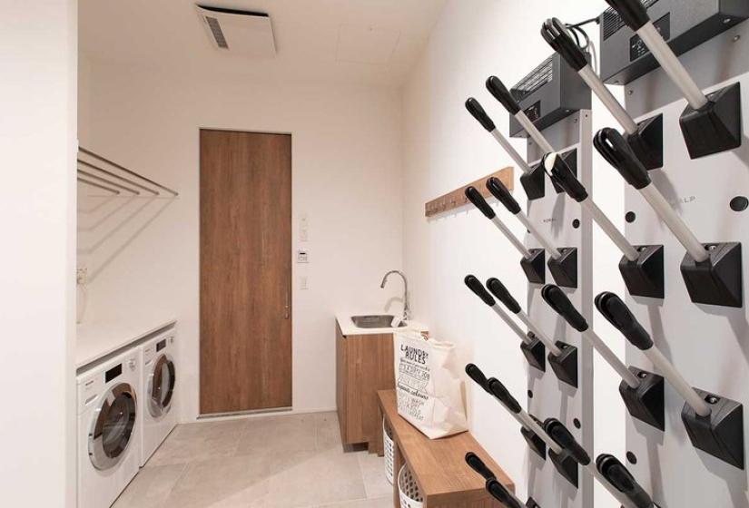 High-end ski equipment room in luxury Niseko chalet featuring custom wall-mounted boot and ski storage system, modern drying facilities, full-size washer and dryer, and polished concrete floors - essential amenities for serious powder enthusiasts visiting Japan's premier ski destination.