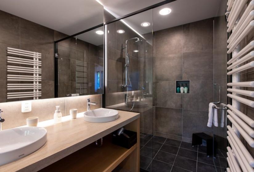 Stylish ensuite bathroom in Chalet Kiraku featuring a glass walk-in shower, double vanity with illuminated mirror, heated towel rack, dark tile flooring, and contemporary fixtures, providing premium comfort for guests at this luxury Niseko ski accommodation.