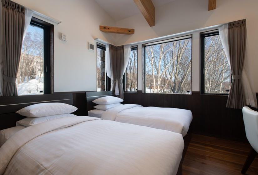 Modern Japanese-inspired bathing area in Chalet Kiraku featuring a sunken concrete soaking tub with wooden steps, minimalist design with concrete walls, ambient lighting, and clean aesthetic, offering a serene relaxation retreat after skiing in Niseko.