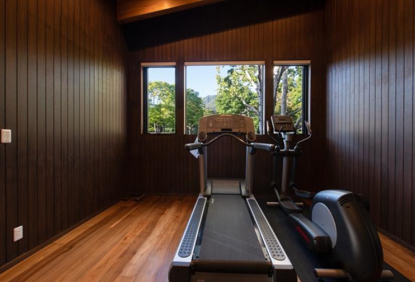 Intimate wood-paneled gym in Chalet Kiraku featuring a treadmill and exercise bike positioned in front of large windows offering forest and mountain views, providing guests with exclusive fitness facilities during their luxury Niseko ski holiday.