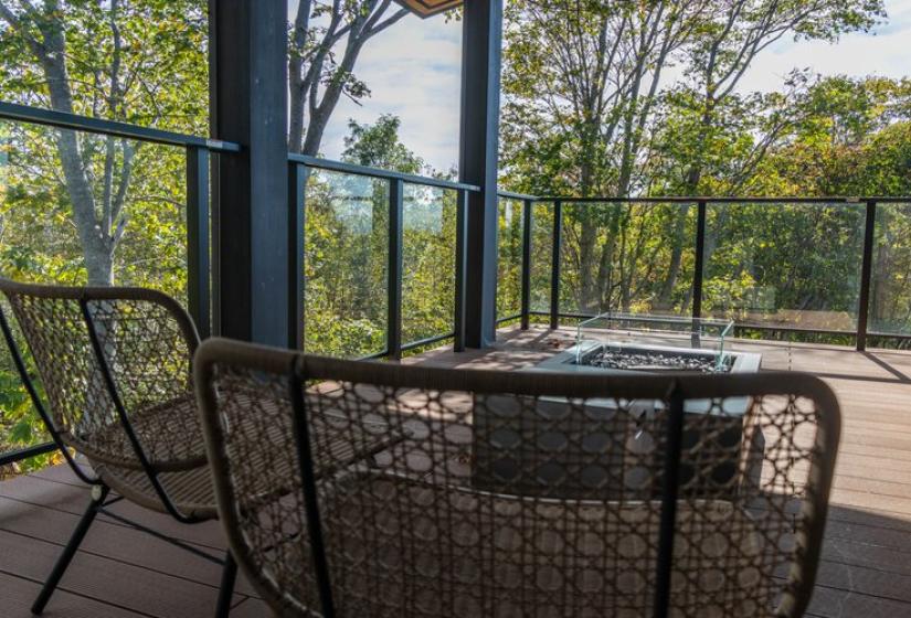 Luxury outdoor deck area at Chalet Lotus Niseko featuring a circular firepit with seating, glass railings, and panoramic views of the surrounding lush forest, perfect for relaxing after a day on the slopes.