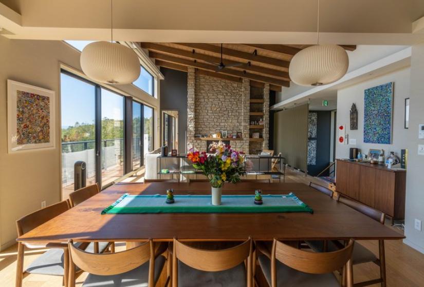 Stylish dining area in Chalet Lotus Niseko with large wooden table seating eight guests, contemporary pendant lighting, exposed wooden beams, floor-to-ceiling windows with mountain views, and modern décor for luxury alpine dining experiences.