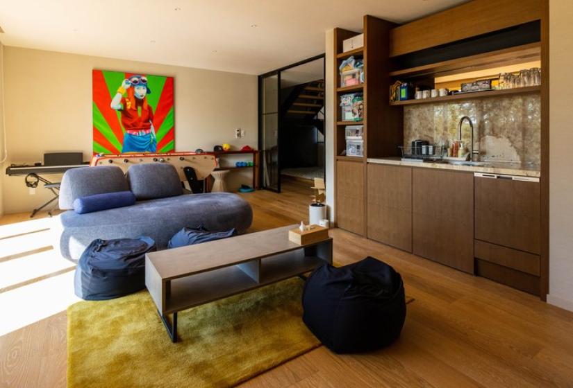 Modern living room interior of Chalet Lotus Niseko featuring a blue sofa, wooden coffee table, vibrant colorful artwork, and a stylish built-in bar area, showcasing the luxury accommodation's premium design and comfort.