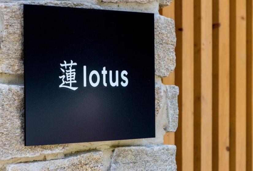 Elegant sign for Chalet Lotus Niseko featuring Japanese kanji and "lotus" text on black background, mounted on stone wall with wooden paneling, representing premium ski accommodation in Annupuri Village.