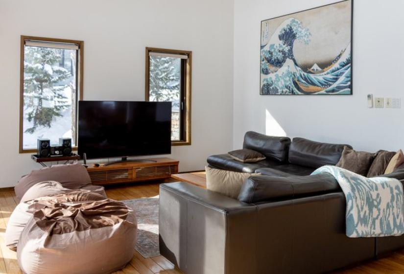 Modern living room in Chalet Snowbird featuring a gray sofa, wooden coffee table, flat-screen TV, and Hokusai's Great Wave artwork on the wall with snowy views through windows.