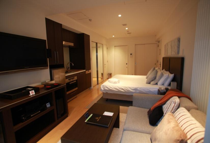 Alpen Ridge Niseko 1 bedroom apartment featuring cozy studio layout with king bed cream sofa flat-screen TV wooden entertainment unit warm lighting wooden flooring and compact living space ideal for couples ski vacation