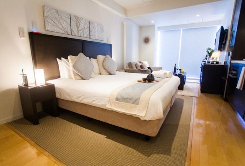 Alpen Ridge Niseko 3 bedroom apartment second bedroom featuring king bed with dark wood frame white premium bedding multiple pillows wooden flooring bedside tables and large windows with natural light