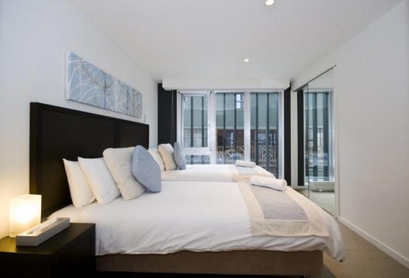Alpen Ridge Niseko 3 bedroom apartment bedroom featuring bed with dark headboard crisp white linens blue accent pillows bedside lamps and floor-to-ceiling windows