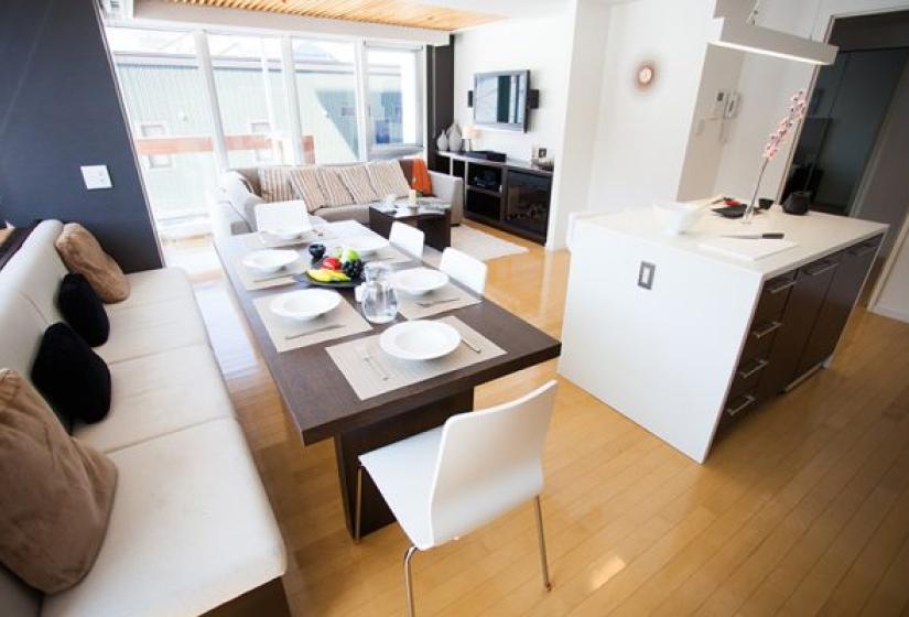 Alpen Ridge Niseko 3 bedroom apartment featuring cozy living space with L-shaped sofa coffee table dining area open-plan kitchen with breakfast bar wooden flooring and bright natural lighting