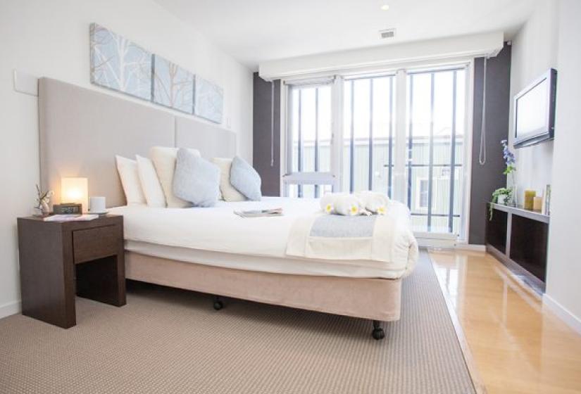 Alpen Ridge Niseko 4 bedroom apartment featuring master bedroom with king bed plush headboard bedside tables ensuite bathroom large windows with mountain views and wooden flooring