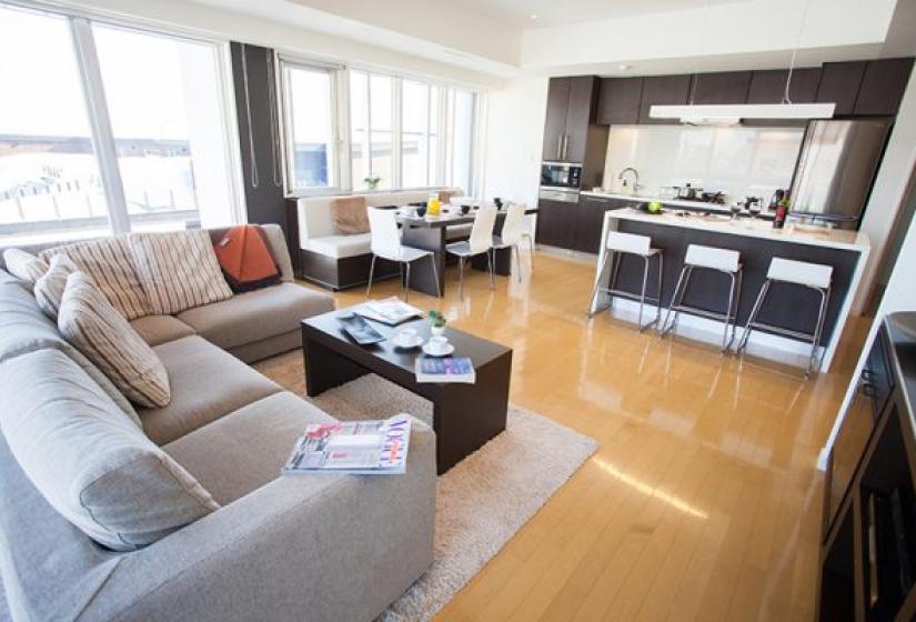 Alpen Ridge Niseko 4 bedroom apartment featuring open-plan living area with comfortable grey sofa coffee table dining space fully equipped modern kitchen wooden flooring and large windows with natural light
