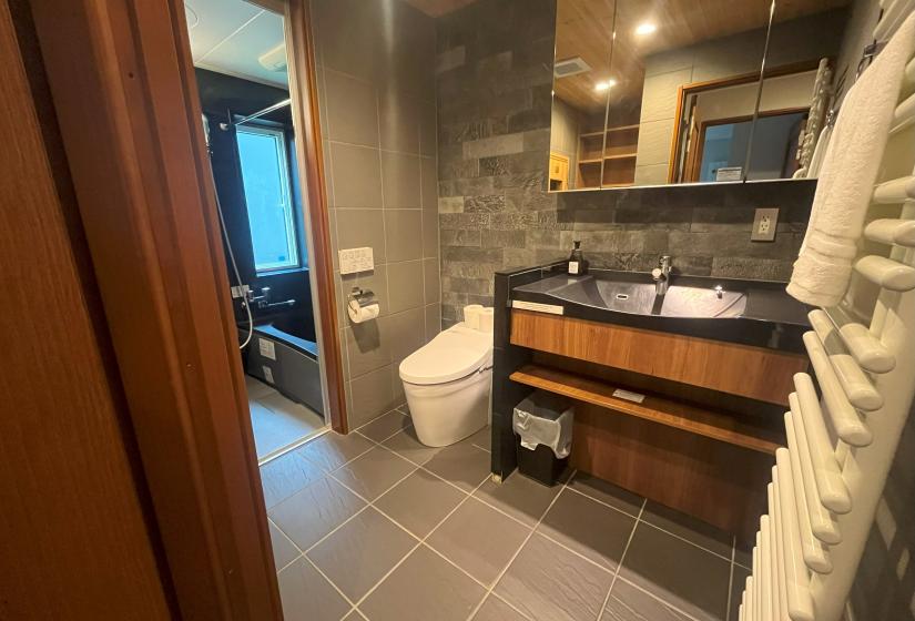 Modern bathroom with wooden vanity, gray tiles and glass shower at Zangetsu Niseko holiday rental