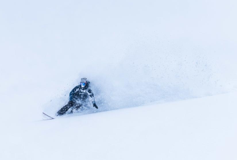 A snowboarder makes a deep turn in the powder